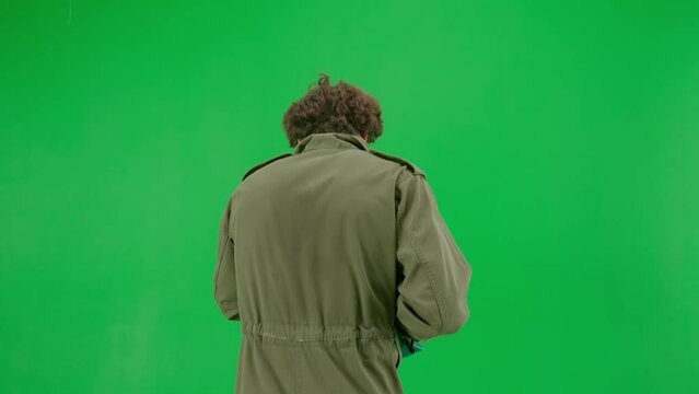 A maniac in overalls runs and swings a chainsaw. An unrecognizable man in the terrifying guise of Jason Voorhees on a green screen chromakey. Halloween, horror. Back view.
