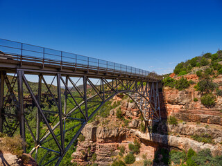 a man sitting on the rocks looking at a bridge in a canyon