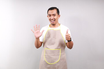 Happy Asian male housekeeper chef cook baker man wear apron showing six fingers isolated on gray...