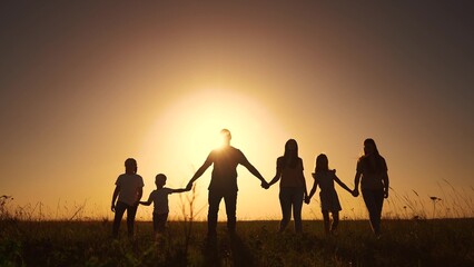 The silhouette family walking in the park. happy family kid dream concept. The family is big and handful of people. big large family silhouette at sunset lifestyle holding hands at sunset in a field