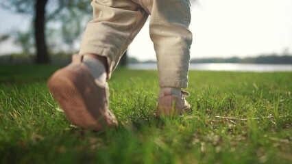 baby walks in the park takes his first steps. happy family kid dream concept. baby legs close-up walking in the park close-up first steps. toddler walks on the grass lifestyle in the park in summer