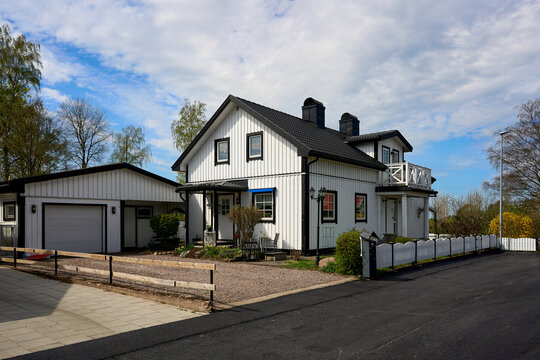 Big beautiful wooden house villa cottage painted white color. Porch and balcony. Black tile roof in contrast color. Garage.