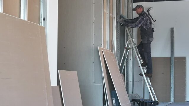 Contractor Worker on Ladder Inside Building. Drywall Wall Construction.