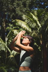 Calm young Hispanic woman holding hands in namaste meditating doing yoga breathing exercises with...