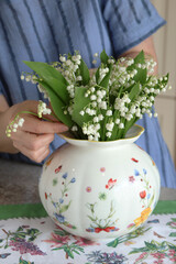 Female put bouquet of lilies of valley in vase