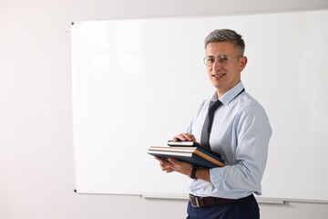 Teacher with notebooks near whiteboard in classroom