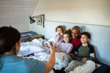 Father and children posing for a picture taken by mother in bed at home