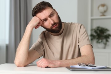 Overwhelmed man suffering from headache at table indoors