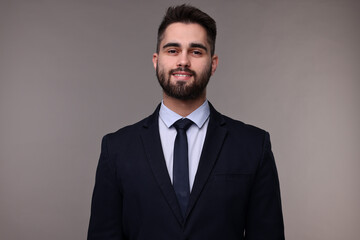 Smiling businessman in suit and necktie on grey background