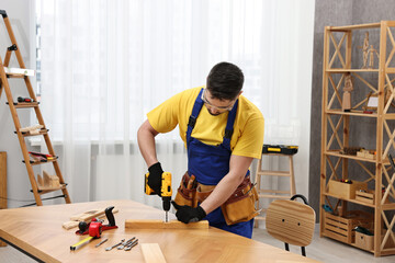 Young worker using electric drill at table in workshop