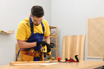Young worker using electric drill at table in workshop