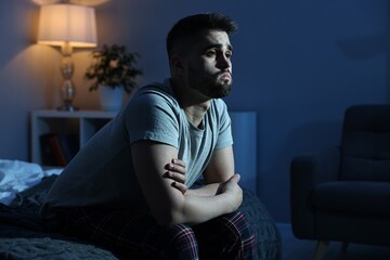 Frustrated man sitting on bed at night