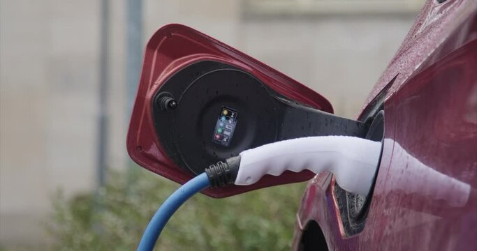 Closeup shot of the process of charging a red electric car on a rainy day in Jena city, Germany