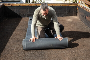 A craftsman rolls out a thick rubber tarpaulin on a flat roof