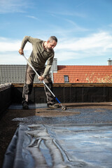 man applies adhesive to an old bitumen sealant and then glues on a rubber sheet