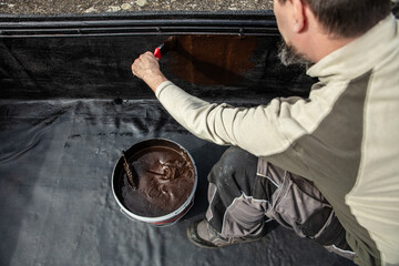 a craftsman applies liquid bitumen  to a roof to seal it