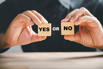 Hand holds Yes and No text on two wooden cubes, symbolizing Yes or No choice. True and false...