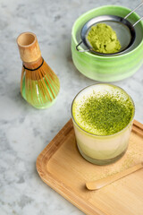 Cup of green matcha with powder on a wooden board.