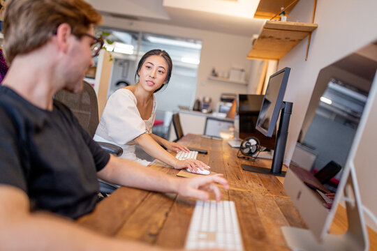 Asian woman and caucasian man sitting at a desk discussing ideas in a creative studio space