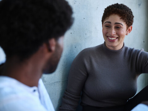 Man and woman sitting against a concrete wall having a conversation