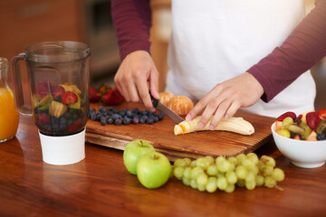 Hands, fruit and prepare with blender on chopping board in kitchen for health or wellness with nutrition. Person, knife and cutting banana for tropical salad with organic food in home for fiber.