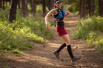 A woman is running through a forest wearing a blue and black backpack
