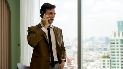 Businessman standing in ornamented office talking on phone with college on cityscape skyline window...