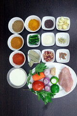 Garlic, cardamom, cinnamon, sariya, semolina, almonds, chart masala, green chillies, bay leaf, coriander, turmeric, chilli, butter, milk, tomato, onion, lemon, ginger, mint, chicken are arranged.