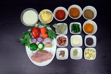 Garlic, cardamom, cinnamon, sariya, semolina, almonds, chart masala, green chillies, bay leaf, coriander, turmeric, chilli, butter, milk, tomato, onion, lemon, ginger, mint, chicken are arranged.