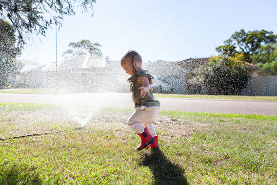Aussie kid running through sprinkler in bright sunlight