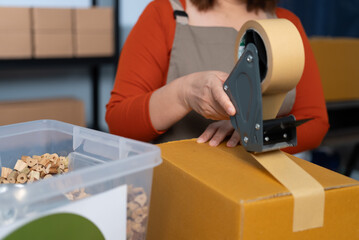 A woman using kraft paper tape to seal a cardboard box in a home-based business, highlighting eco-friendly packaging and sustainable practices in small business operations