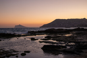 Fototapeta premium Sunset in Cala del Morelló next to the Torre del Molí, with views of the Peñón de Ifach, Banys de la Reina ,Roman-era structures, Calpe, Costa Blanca Alicante, Spain.