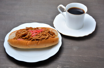 白い皿に乗ったおいしそうな焼きそばパンとコーヒー