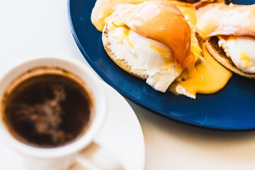 Egg Benedict with salmon and hollandaise sauce on a blue plate with a cup of freshly brewed coffee....