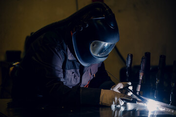 Man worker working with a metal product and welding it with a arc welding machine in a workshop. Industrial manufacturing. Welding metal part in a factory.
