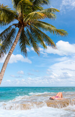 A young girl sunbathing on a rock next to a crooked palm tree - Cancun, Mexico