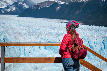 Mujer turista con campera y mochila roja disfrutando de las vistas del Glaciar Perito Moreno, en la...