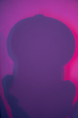 A close-up silhouette of a woman in a hat, diffused light. Abstract gradient pink and purple background with a woman's shadow. High quality photo