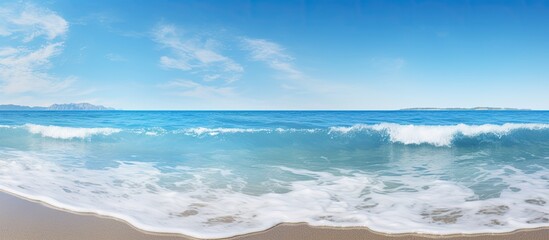During a sunny summer morning calm blue waves splash on the seashore and beach under a clear sky creating a scenic copy space image