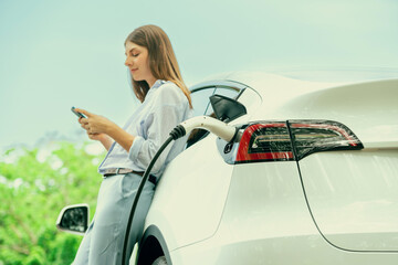 Young woman using smartphone online banking application to pay for electric car battery charging...