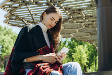 Young beautiful woman in jeans and poncho looking at phone.