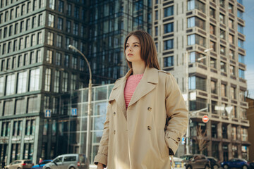 A young beautiful woman in a beige trench coat on the background of a business building.