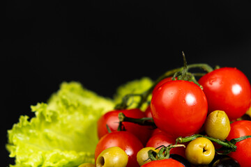 Cherry tomatoes with green olives on lettuce leaf on black background with space for text copy space