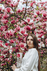 A young woman in a white shirt has come out of the office and is enjoying blooming magnolias.