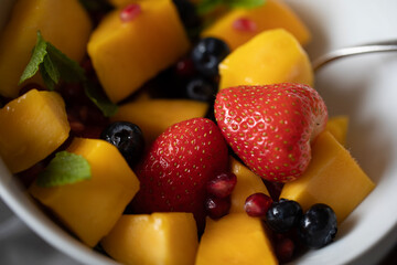 COLOURFUL FRESH FRUIT SALAD WITH MINT LEAVES CLOSE UP IN WHITE BOWL
