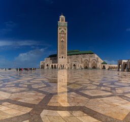 view of the exterior and the minaret of the Hassan II Mosque in casablanca with reflections on the wet marble in the foreground