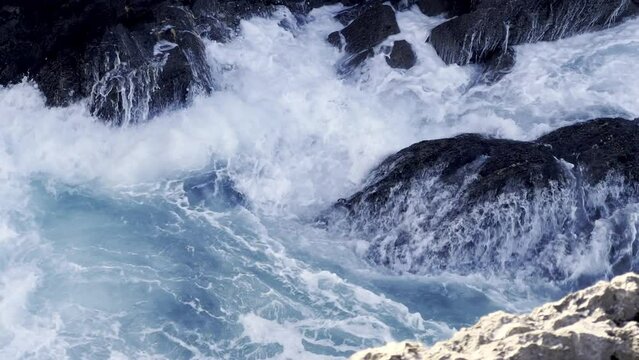 High angle shot of a rocky cliff, with waves crashing in slow motion. Travel, nature and wallpaper concept.