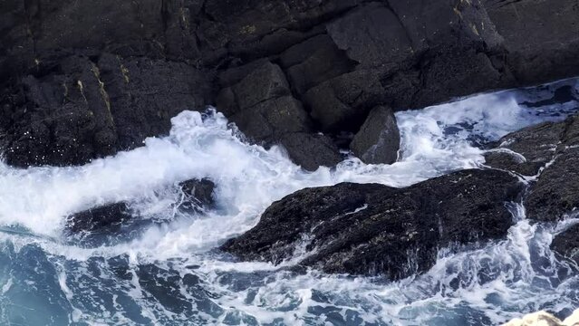 High angle shot of a rocky cliff, with waves crashing in slow motion. Travel, nature and wallpaper concept.