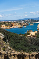 Fototapeta premium Ponta da Piedade near Lagos in Algarve, Portugal. Cliff rocks and tourist boat on sea. Praia Dona Ana, Estudantes beach. Sunny day. Point of Pity