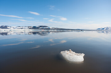 A wide low angle view of melting sea ice floes in still waters of Northern Arctic with mountains...